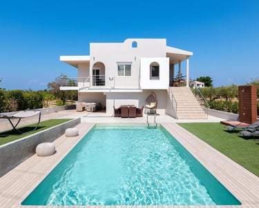 Luxury white villa with a private swimming pool, sun loungers, and outdoor patio under a clear blue sky.