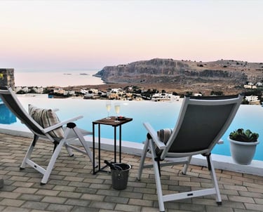 Luxury villa terrace with infinity pool overlooking Lindos, Greece at sunset.
