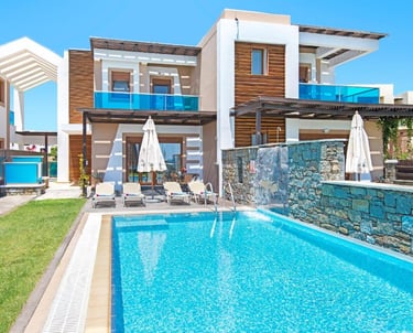 Luxury modern villa with private swimming pool, stone waterfall feature, and sun loungers.