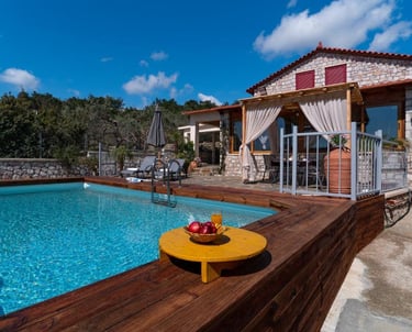 Luxury stone villa with a private swimming pool, wooden deck, and outdoor patio under a blue sky.
