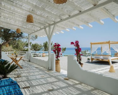 Luxury white beach resort terrace with canopy bed, rustic pergola, and sea view.