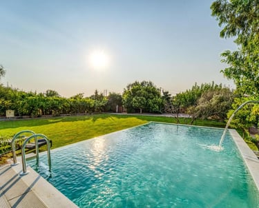 Luxury infinity pool with a waterfall feature overlooking a lush green garden at sunset.