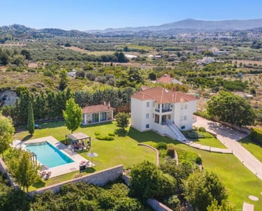 Aerial view of a luxury villa with a private swimming pool and garden in a Greek landscape.