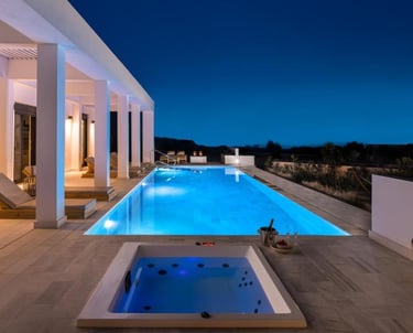 Luxury villa terrace at night featuring a lit swimming pool and a modern outdoor hot tub.