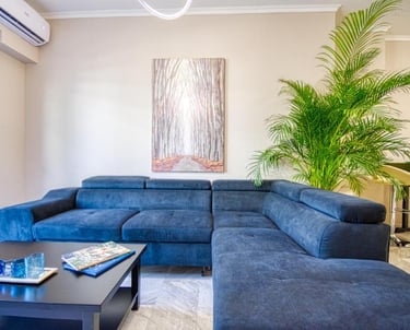 Modern living room featuring a blue sectional sofa, a large palm plant, and forest wall art.