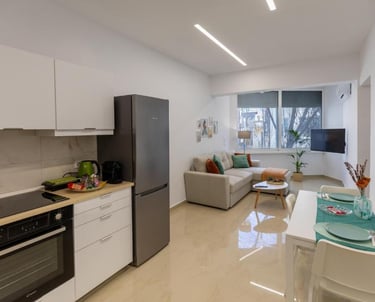 Modern open-plan apartment featuring a sleek kitchenette, gray sofa, and white dining table.