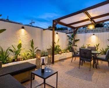 Modern outdoor patio with dining set, wooden pergola, and garden lighting at night.