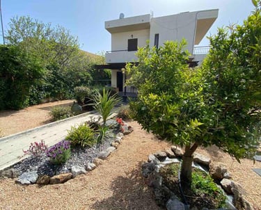 Two-story Mediterranean villa with a gravel courtyard garden and lush green trees.