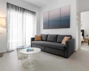 Modern living room featuring a dark grey sofa, round wire coffee tables, and a three-piece ocean wall art.