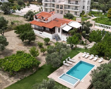 Aerial view of a Mediterranean villa with a swimming pool, sun loungers, and lush green gardens.