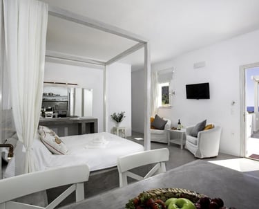 Luxury white hotel suite with a canopy bed, minimalist decor, and a balcony view of the sea.