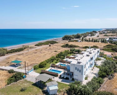 Aerial view of a luxury beachfront villa resort with private pools near a sandy Mediterranean beach.
