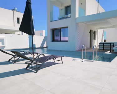 Luxury modern villa with private swimming pool, sun loungers, and black parasol under a clear blue sky.