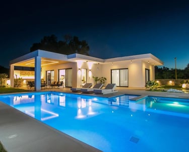 Luxury modern villa at night with a glowing swimming pool and outdoor lounge area.