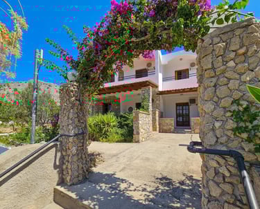 Greek villa entrance with a stone archway covered in blooming purple bougainvillea flowers.