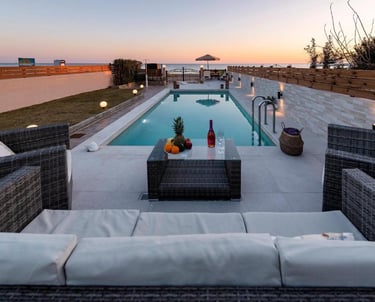 Luxury villa patio with a private swimming pool, rattan lounge furniture, and sunset ocean views.