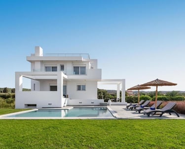 Luxury modern white villa with a private swimming pool, sun loungers, and umbrellas on a green lawn.