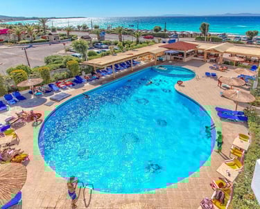 Luxury beach resort with a large outdoor swimming pool, sun loungers, and view of the turquoise Mediterranean sea.