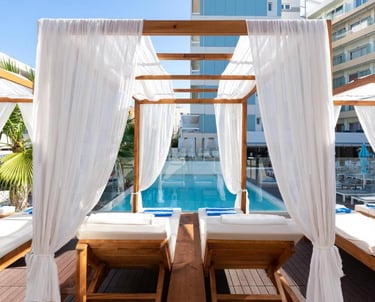 Luxury poolside wooden cabanas with white curtains and sun loungers at a boutique resort hotel.