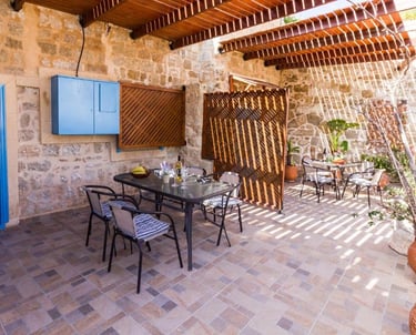 Mediterranean outdoor patio with stone walls, wooden pergola, and dining sets for al fresco meals.