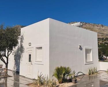 Modern white minimalist villa with a tiled terrace and olive trees under a clear blue sky.