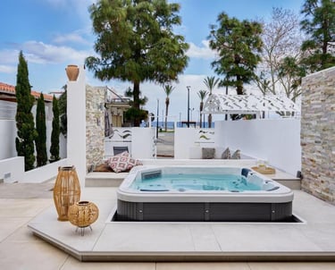 Luxury outdoor patio featuring a modern hot tub, white stone walls, and Mediterranean landscaping.