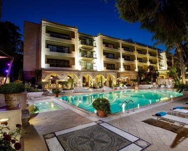 Luxury hotel exterior at night with illuminated swimming pool and sun loungers.