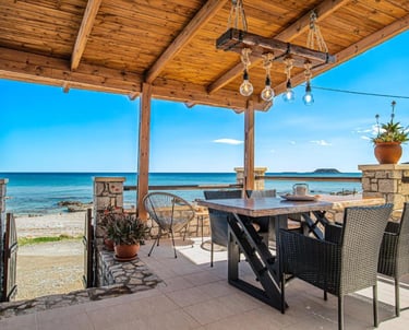 Rustic outdoor patio with wooden pergola, dining table, and ocean view in a seaside villa.