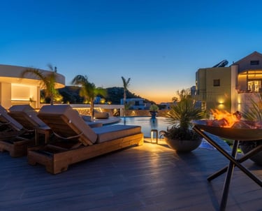 Luxury resort pool deck at sunset with wooden sun loungers, an infinity pool, and a modern fire pit.