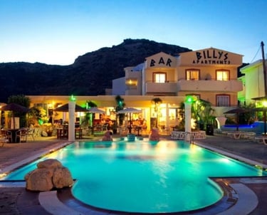 Illuminated swimming pool at Billy's Apartments and Bar in Greece at twilight.