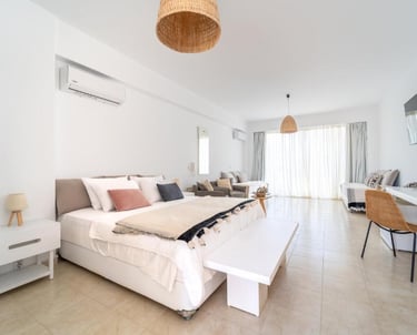 Modern white hotel suite with a king-size bed, air conditioning, and a bright living area.