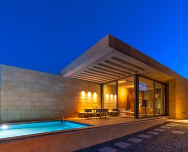 Modern luxury villa at dusk with an outdoor swimming pool, patio dining, and warm interior lighting.