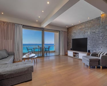 Modern living room with a stone wall, grey sofa, and balcony overlooking the blue ocean.