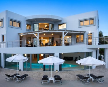 Luxury modern villa with swimming pool, sun loungers, and white umbrellas at dusk.