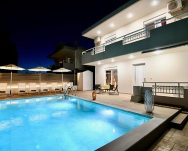 Luxury villa rental with illuminated private swimming pool and sun loungers at night.