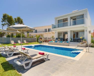Luxury villa with a private swimming pool, sun loungers, and outdoor patio area under a blue sky.