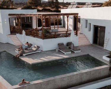 Luxury white villa in Greece with an outdoor infinity pool, wooden pergola, and sun loungers.