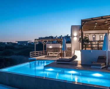 Luxury villa at twilight featuring a lit infinity pool and outdoor patio with lounge chairs.