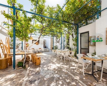 Sun-drenched Mediterranean outdoor restaurant patio featuring a lush lemon tree canopy and stone flooring.