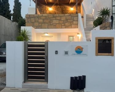 Modern white vacation rental with a stone balcony and wooden pergola at dusk in Greece.