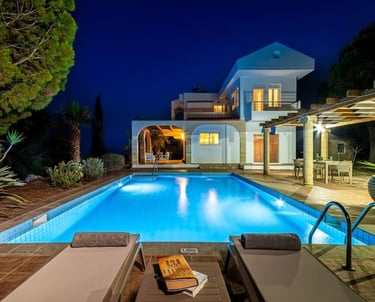 Luxury villa with an illuminated outdoor swimming pool and sun loungers at night.