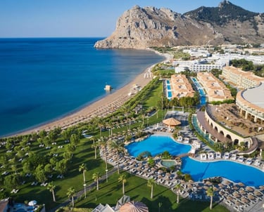 Aerial view of a luxury beachfront resort in Rhodes, Greece with swimming pools and sandy beach.
