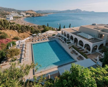 Luxury resort swimming pool overlooking a Mediterranean bay and beach at sunset.