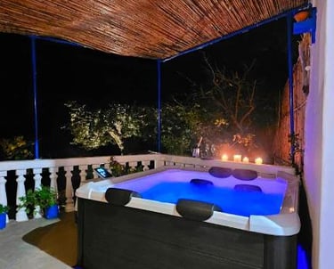 Luxury outdoor hot tub with blue LED lighting under a bamboo roof at night with candles.