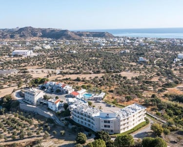 Aerial view of a white luxury hotel resort nestled in a lush olive grove overlooking the Mediterranean coast.