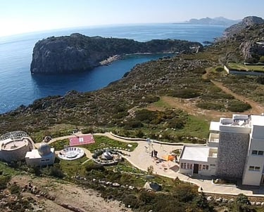 Aerial view of a coastal observatory and villa on a rocky cliff overlooking the Aegean Sea.