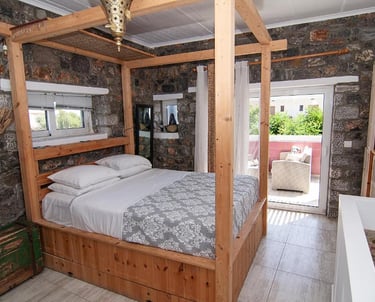 Rustic bedroom featuring a wooden canopy bed, stone walls, and a private balcony.