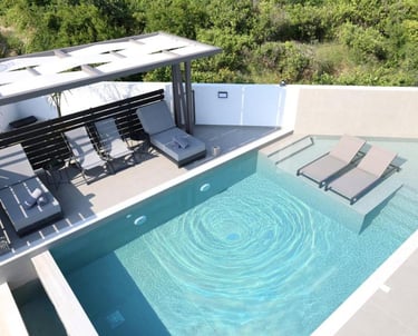 Modern luxury infinity pool with sun loungers and a pergola on a private terrace overlooking green hills.