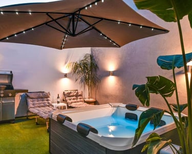 Modern outdoor patio with hot tub, gas grill, and lighted umbrella for luxury backyard relaxation.