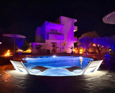 Luxury villa with swimming pool at night featuring purple ambient lighting and lounge chairs.